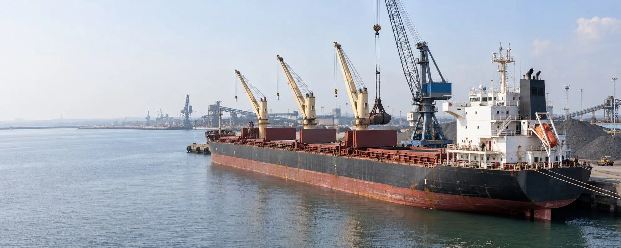 Illustration of a bulk carrier alongside a working berth with a harbour grab crane