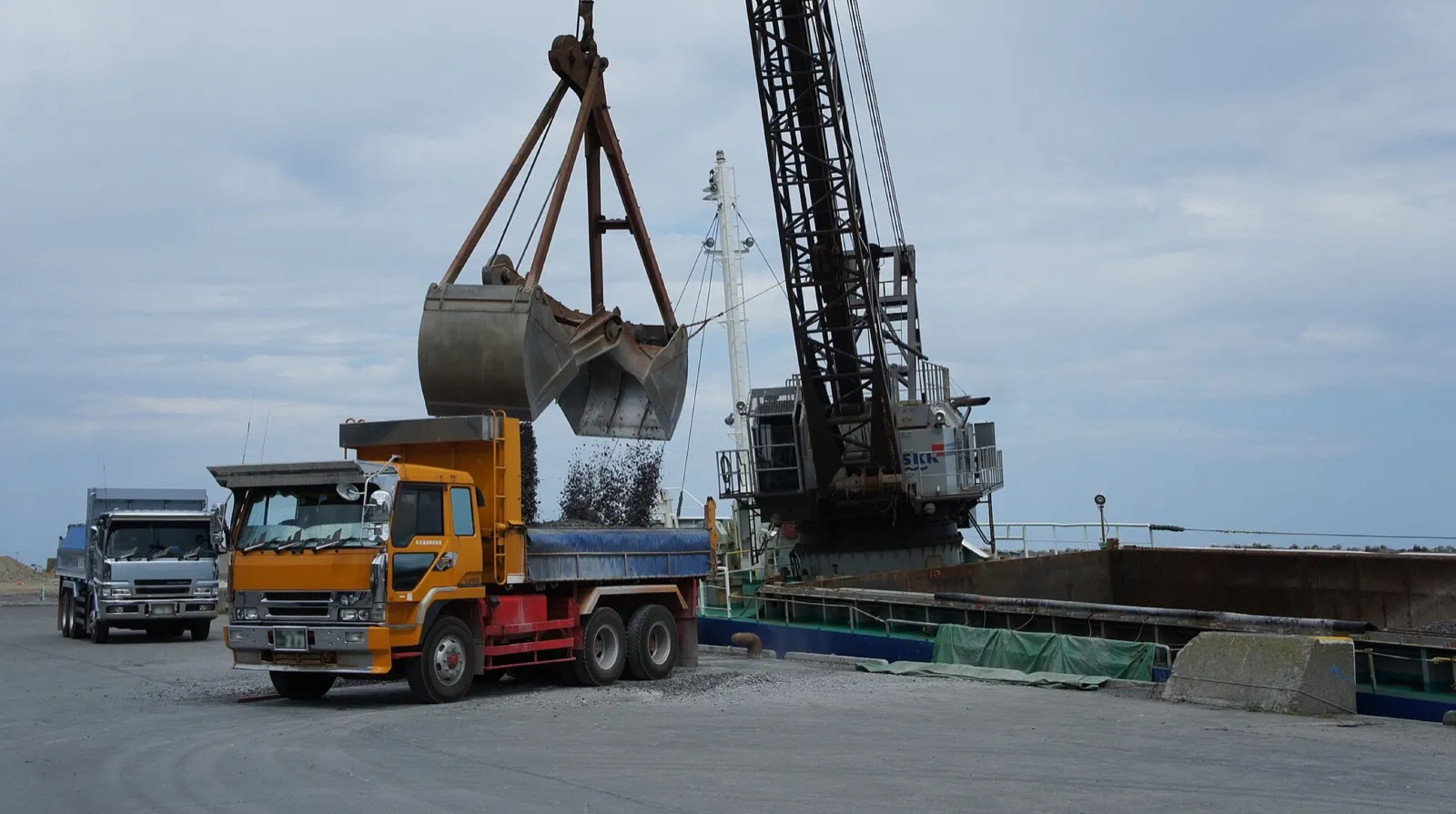 A grab discharging bulk cargo into a tipper truck on the quay